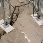 Scaffold screw jacks and base plates seated on timber mudsills over uneven, eroded soil beside a foundation wall